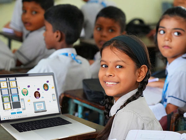 Student sitting in a classroom with a laptop displaying an educational activity, surrounded by her classmates.